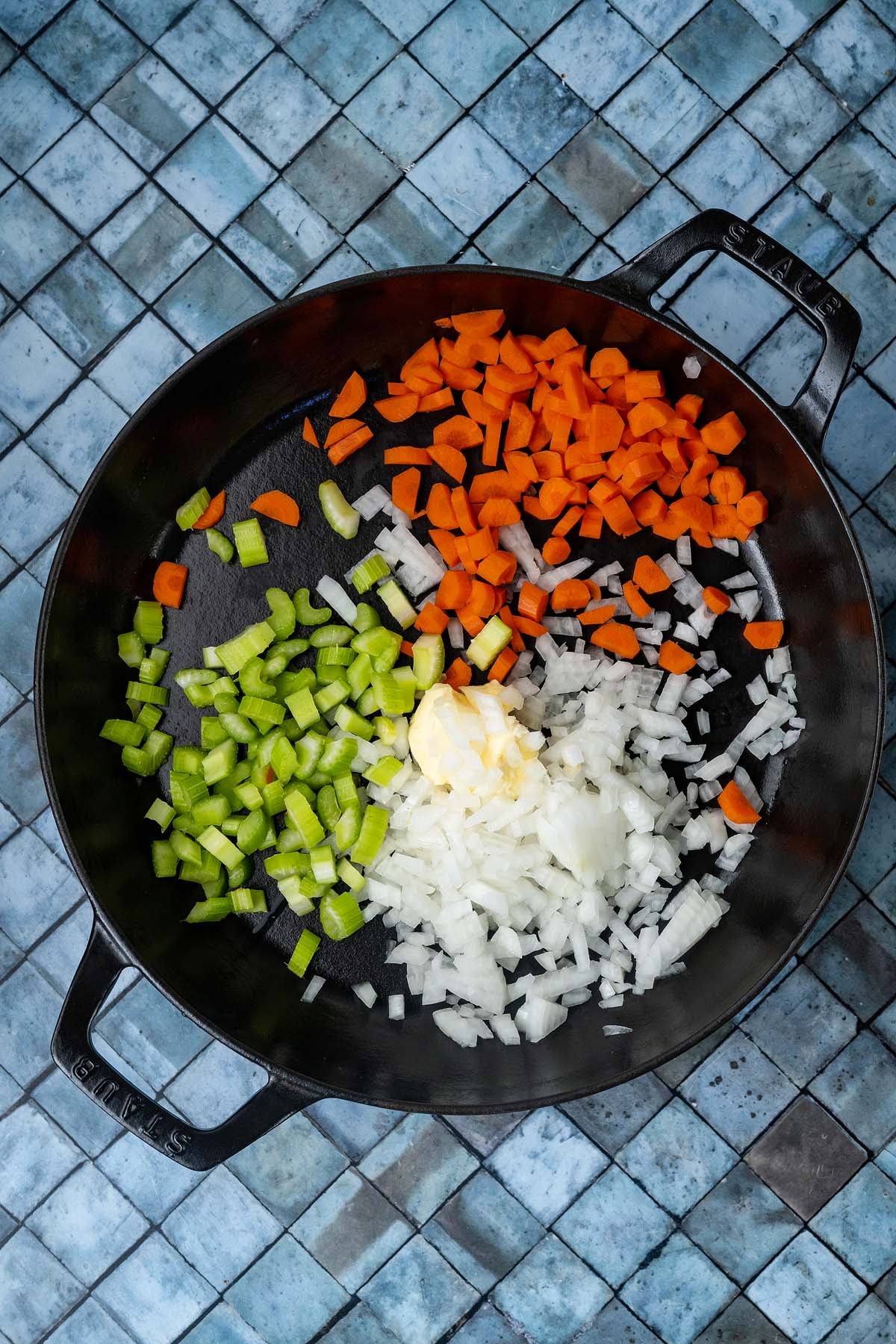 Cast iron skillet containing chopped carrots, celery, onions, and a pat of butter.