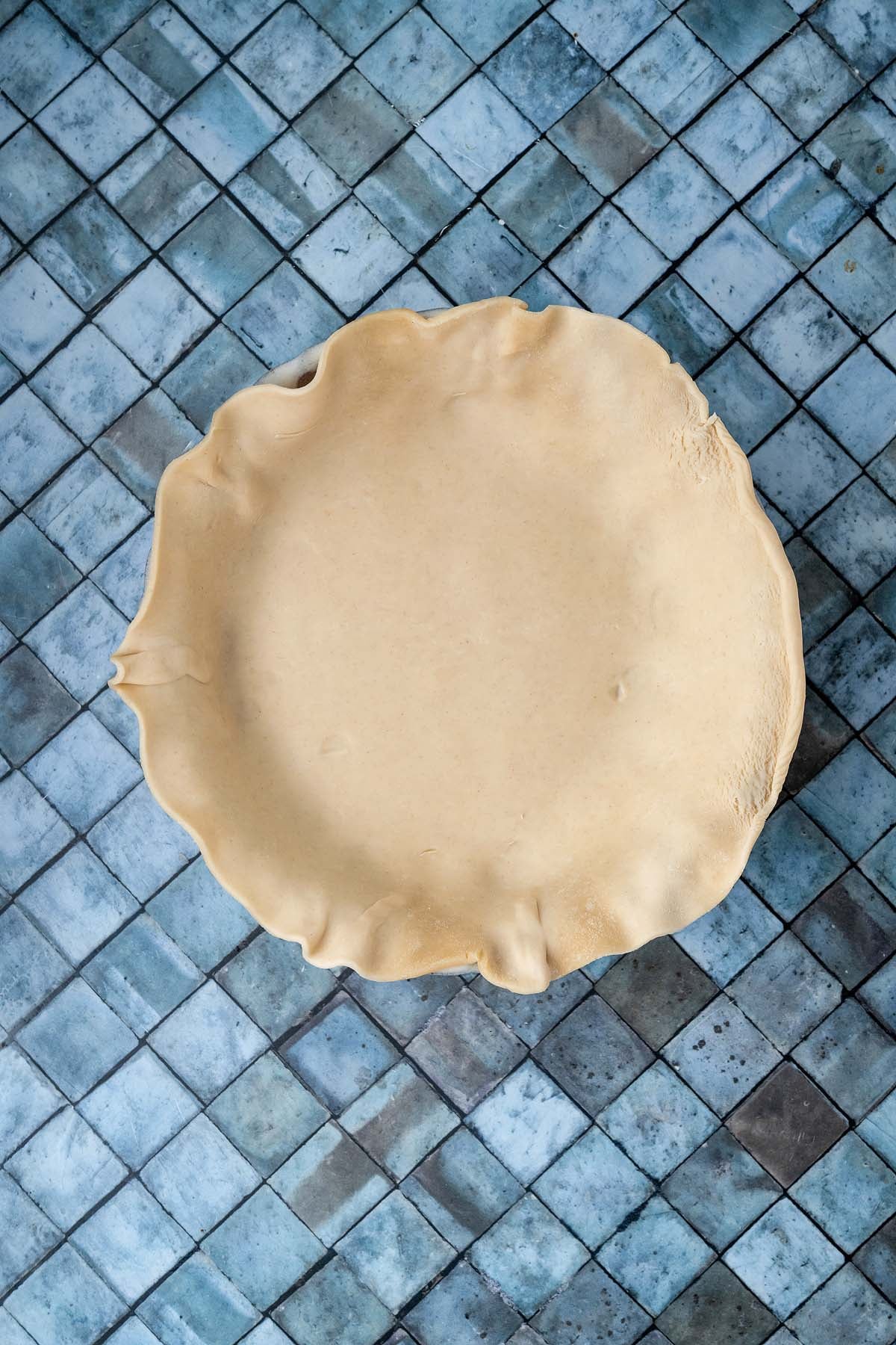 An uncooked pie crust in a metal pan centered on a blue tiled surface.