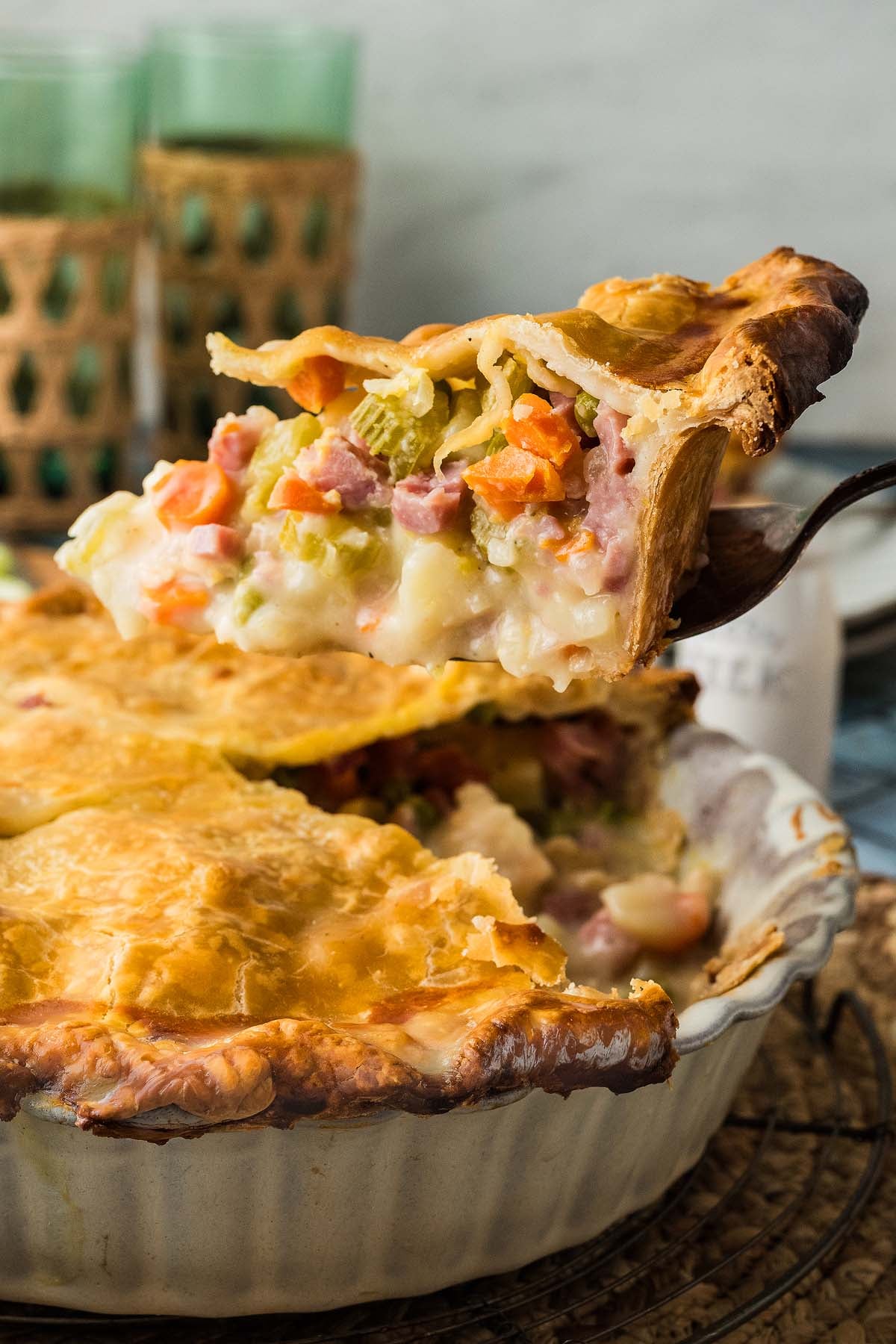 A slice of ham pot pie being lifted from a ceramic baking dish.