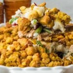 A wooden spoon lifting a scoop of stuffing, turkey, and green bean casserole from a baking dish.