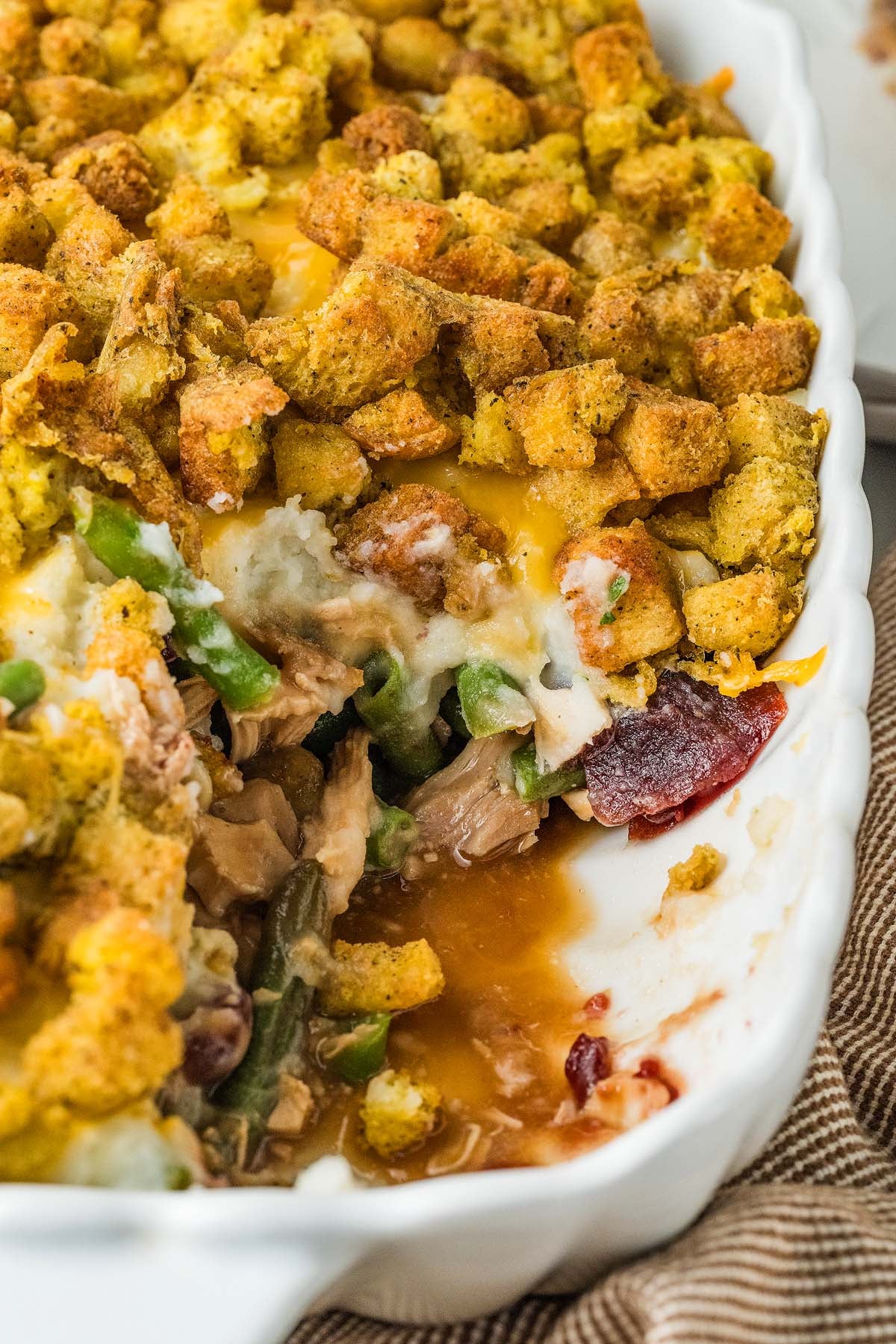 A casserole topped with leftover stuffing, containing leftover turkey, green beans, and cranberry sauce.