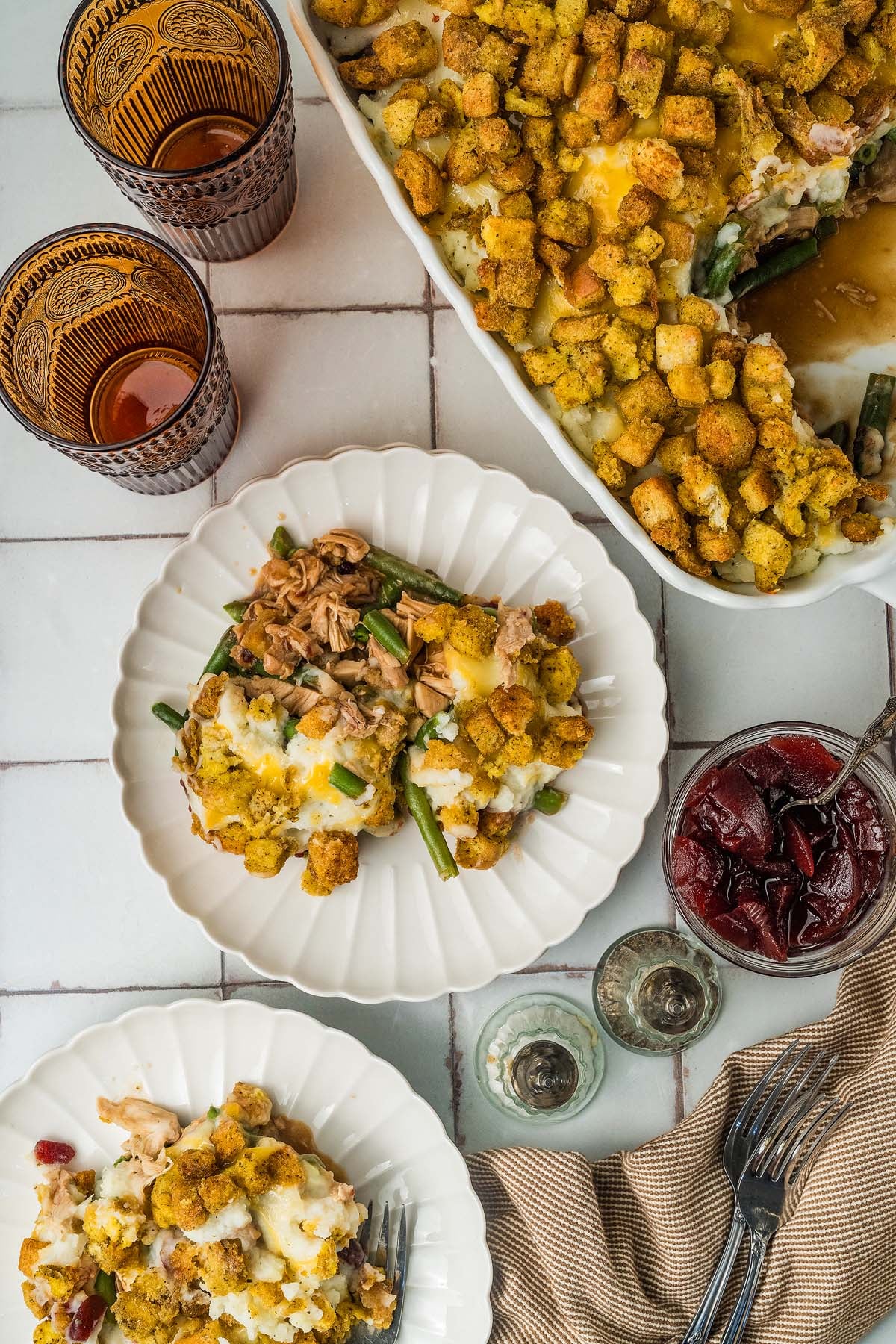 Casserole with shredded turkey, green beans, and stuffing, served on plates with a side of cranberry sauce.