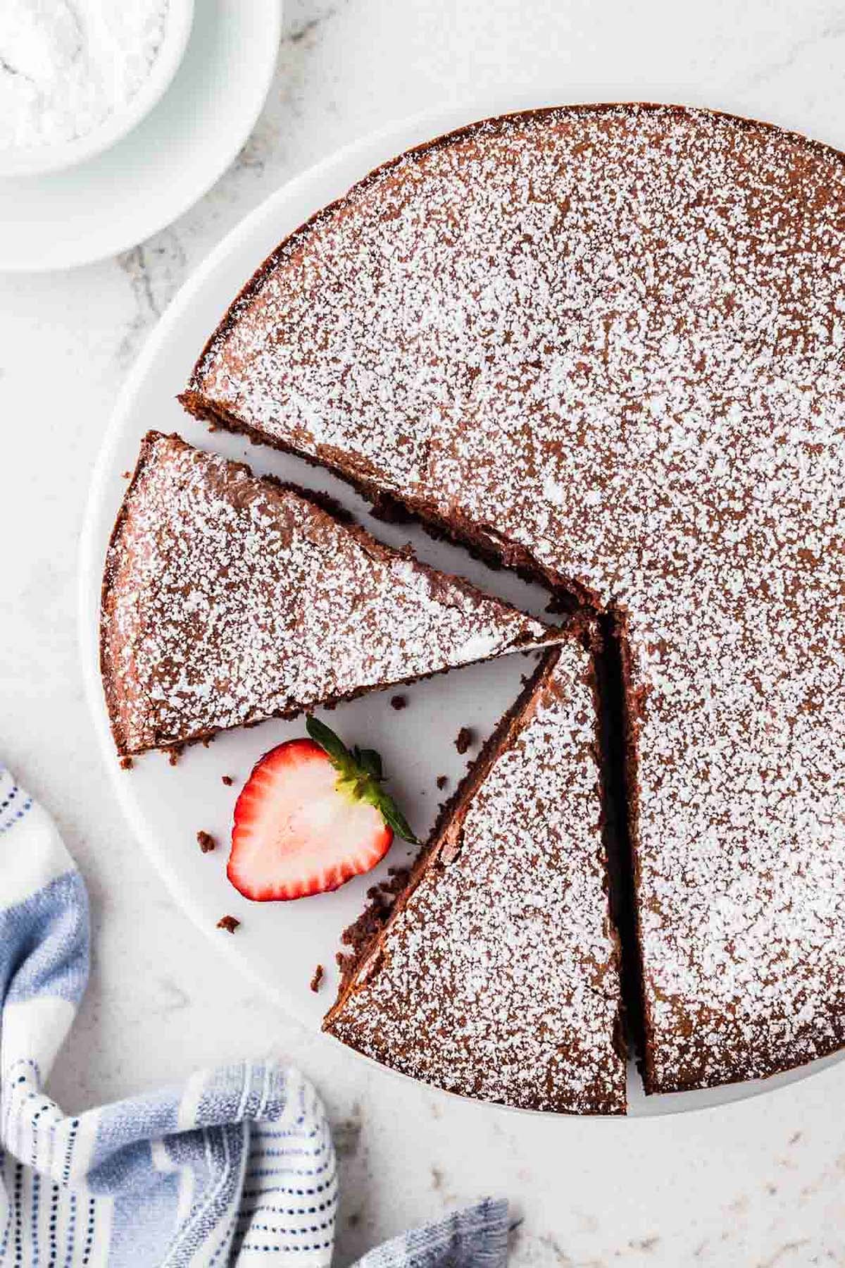 Chocolate flourless italian cake dusted with powdered sugar, served with a strawberry slice.