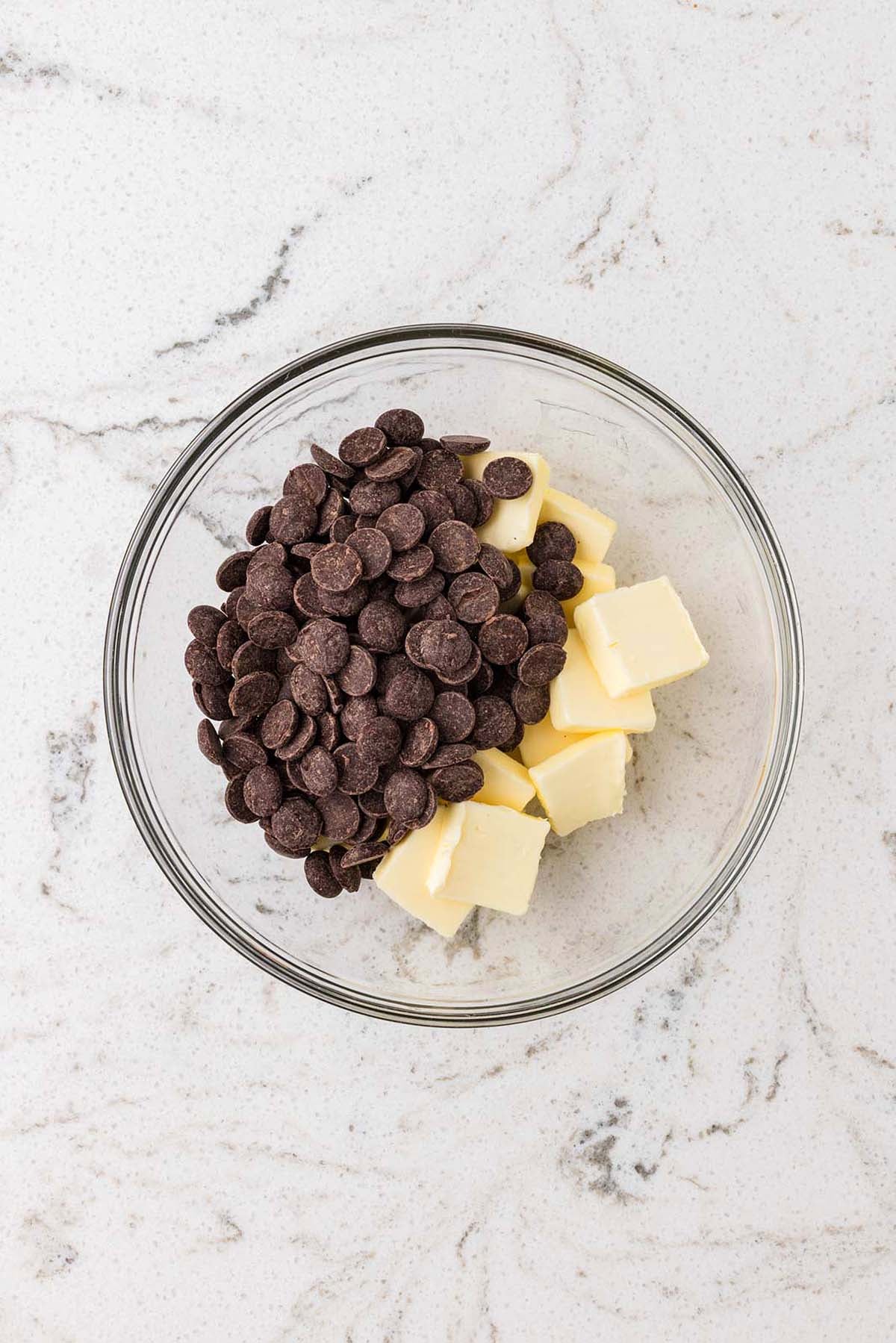 A glass bowl containing chocolate chips and cubes of butter.