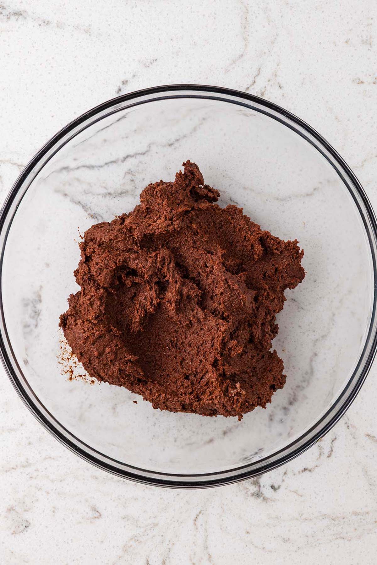 A glass bowl containing a mound of raw chocolate dough.