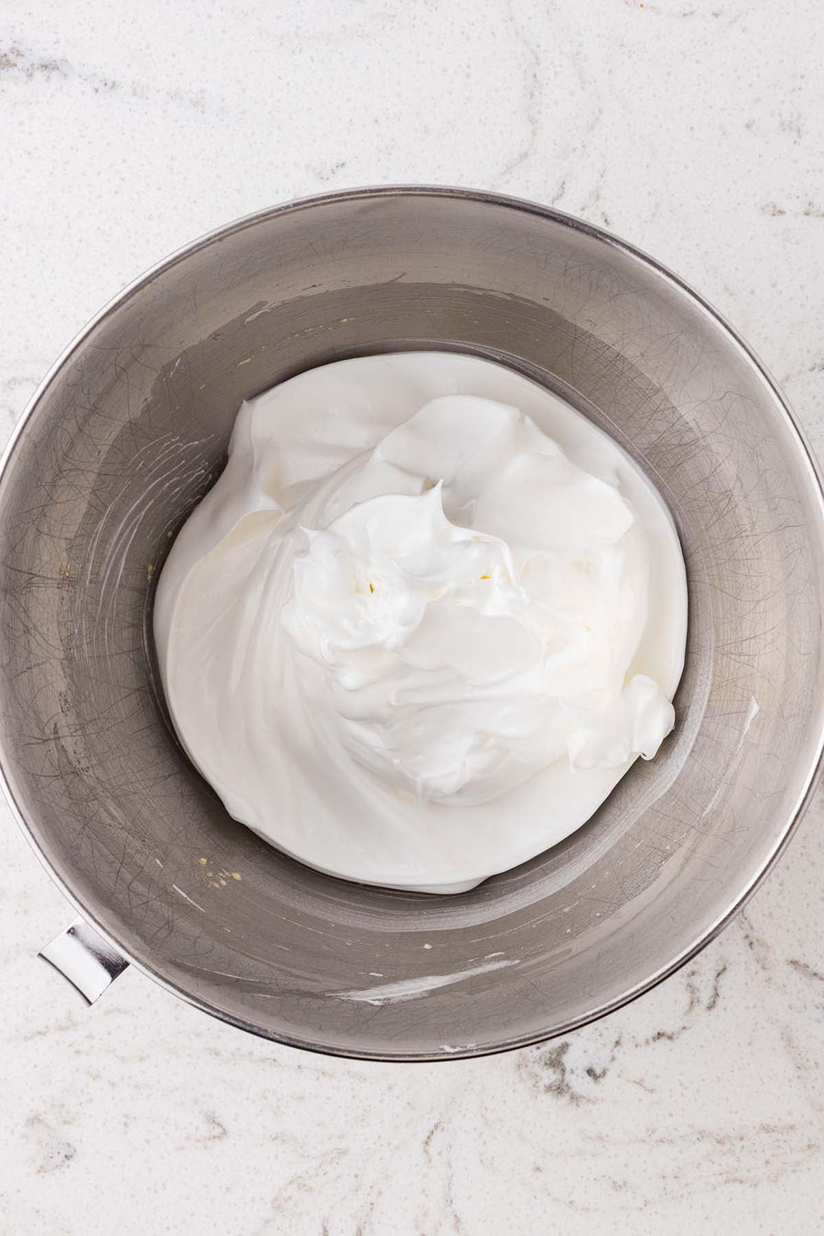 Stiffly whipped egg whites in a stainless steel mixing bowl.