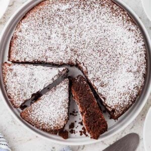 A round Italian chocolate torta caprese cake dusted with powdered sugar.